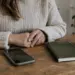 Ruke odrasle žene uz telefon i zatvorenu bilježnicu u neutralnoj prostoriji.
